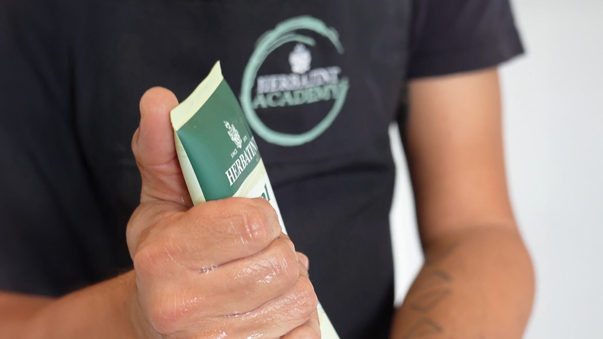 Primo piano del petto del master colorist dell’azienda mentre utilizza prodotti del brand; sulla maglietta nera è visibile il logo dell’academy aziendale
