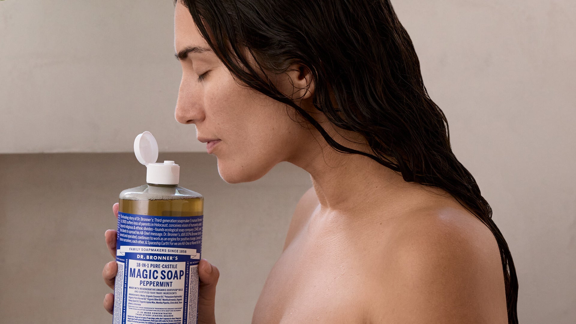 Donna con capelli neri e occhi chiusi che annusa il sapone liquido alla menta Dr. Bronner's Magic Soap Peppermint, con espressione serena
