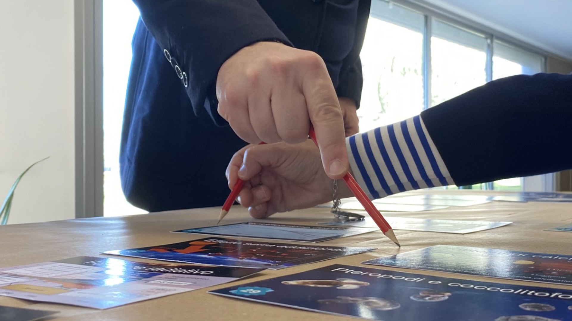 Close-up of two hands each holding a pencil while writing during a corporate team-building activity, on a bright neutral background