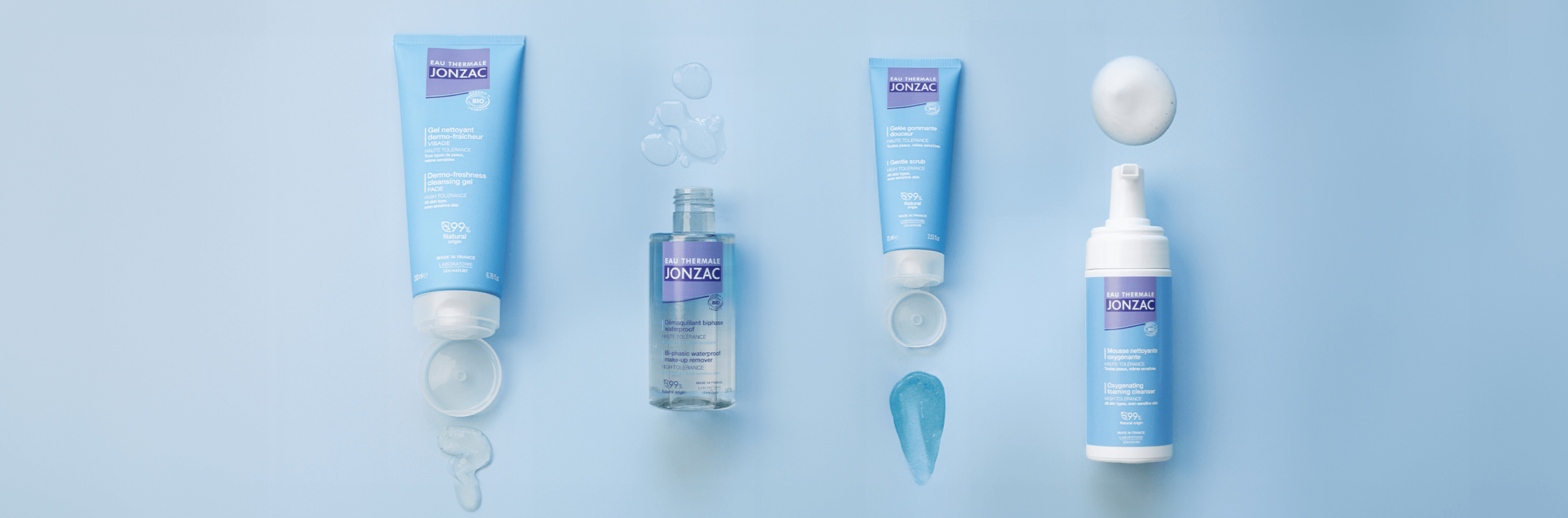 Blue surface displaying four essential Eau Thermale Jonzac products arranged professionally from left to right: dermo-freshness facial cleansing gel, waterproof bifacial makeup remover, shower exfoliating scrub, and oxygénante cleansing mousse